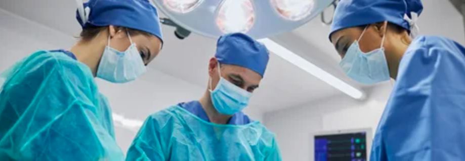 Three surgeons wearing blue scrubs and surgical masks, focused and ready for a surgical procedure in a sterile environment.