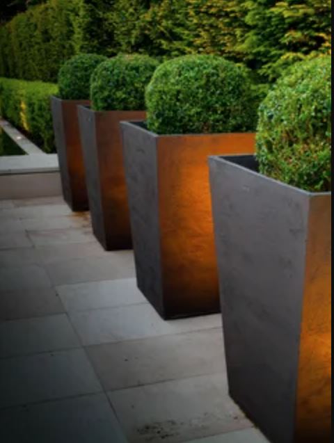 Three large planters illuminated by lights, showcasing vibrant plants in a stylish outdoor setting.