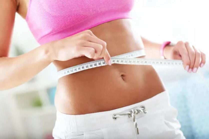 A woman measuring her waist with a tape measure, focusing on her health and fitness goals.