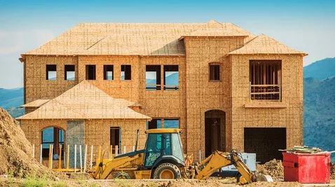 A house under construction, featuring a bulldozer and a tractor on the site, indicating active building progress.