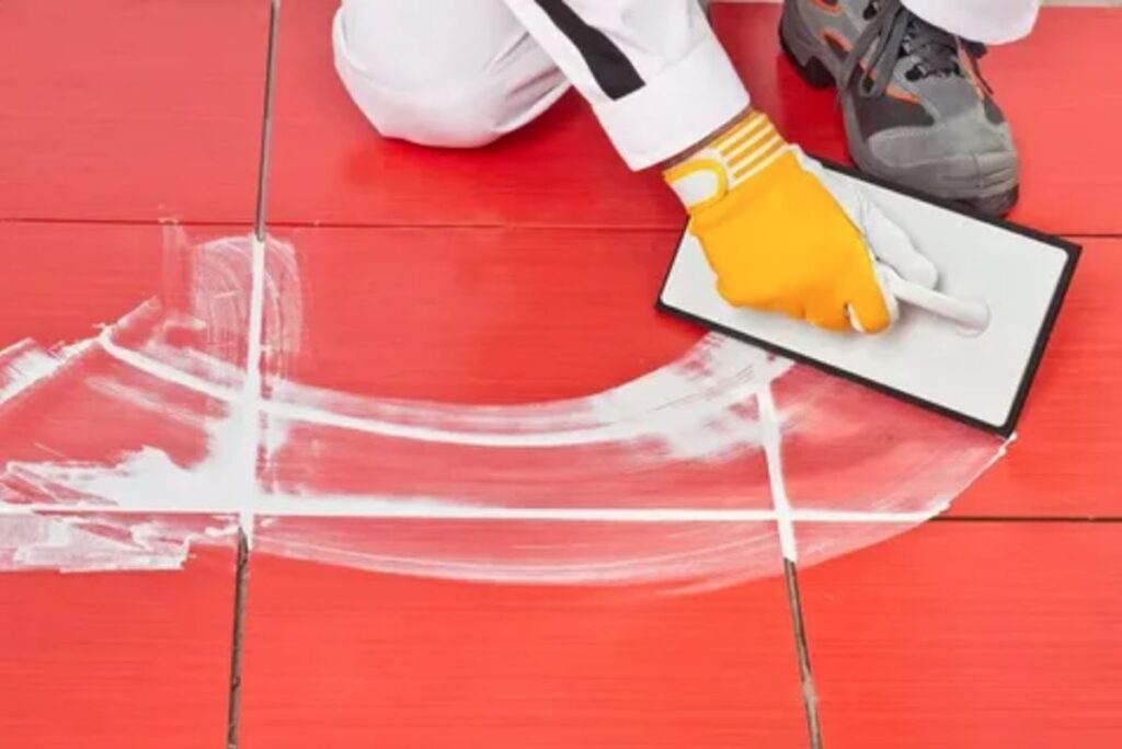 A person applies white paint to a red tile using a brush, showcasing a creative painting process.