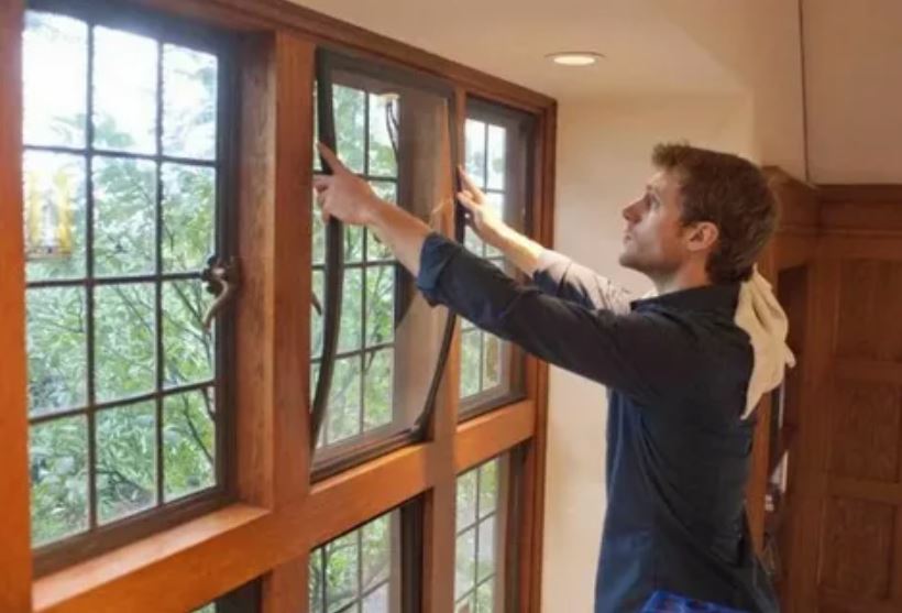 A man installing a window screen onto a window, ensuring a secure fit for protection and ventilation.